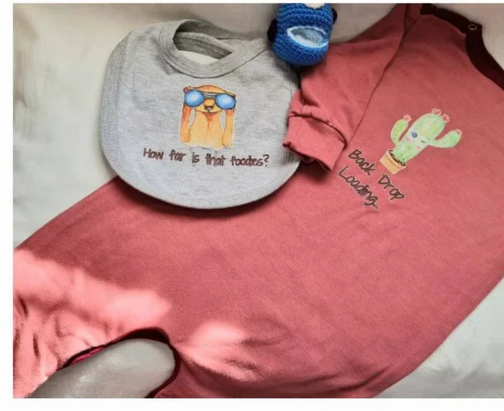 Coral onesie with a cactus print, matching grey bib, and crochet toy